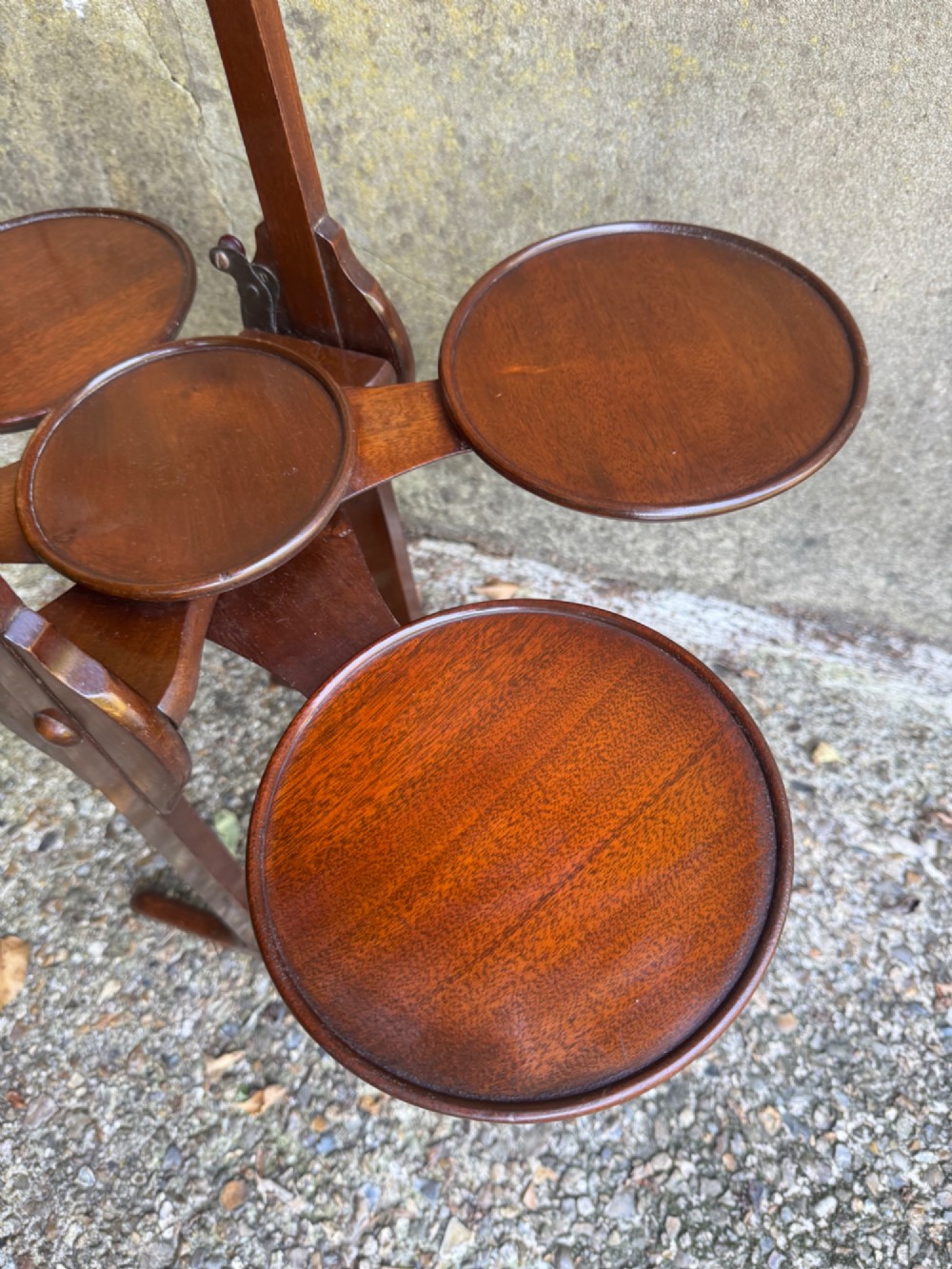 An antique mahogany monoplane folding cake stand with five circular wooden trays supported on a vertical frame with arched feet. View XI