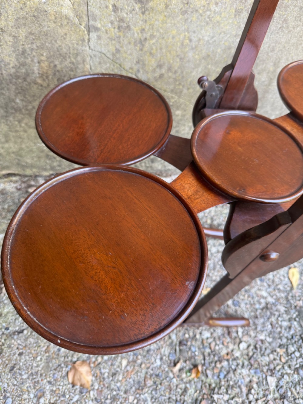 An antique mahogany monoplane folding cake stand with five circular wooden trays supported on a vertical frame with arched feet. View XII