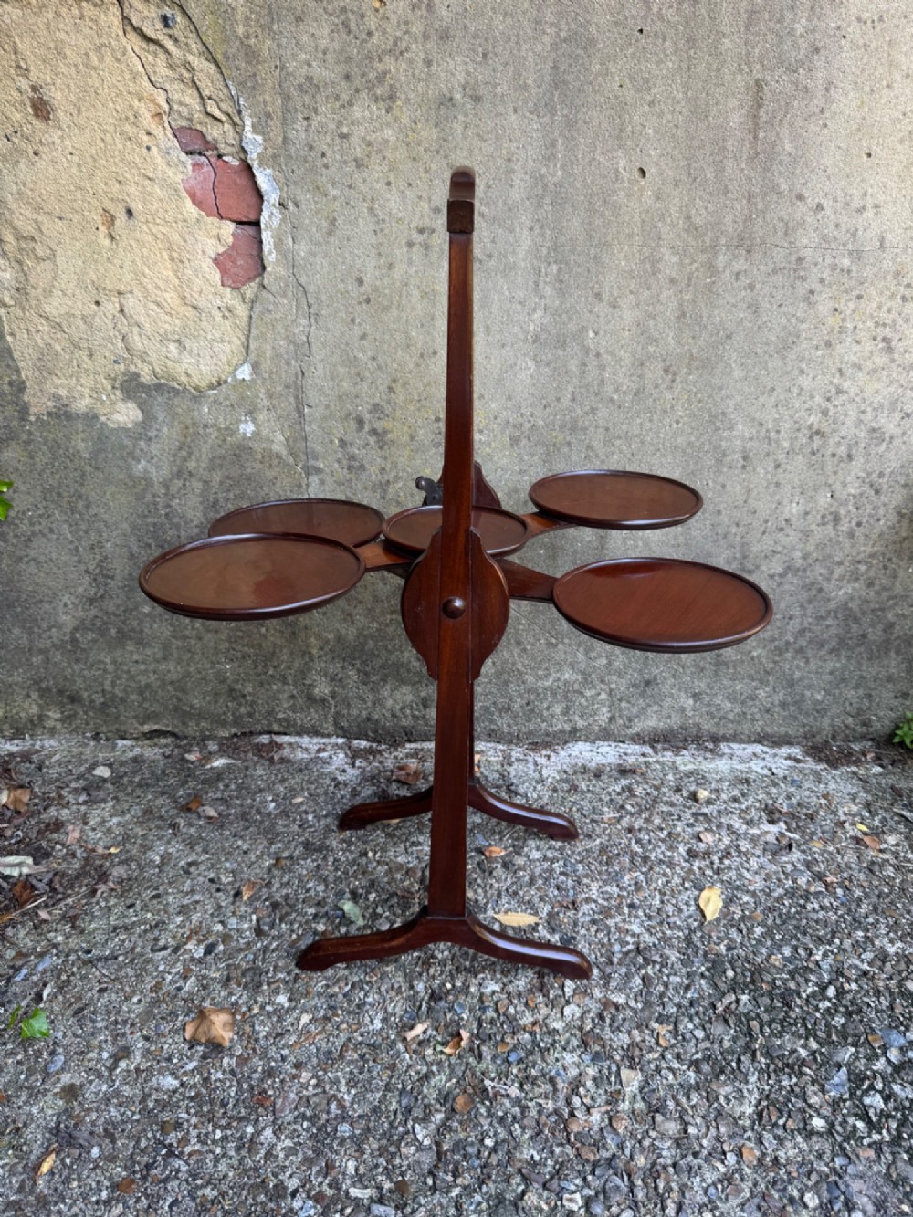 An antique mahogany monoplane folding cake stand with five circular wooden trays supported on a vertical frame with arched feet. View XIV
