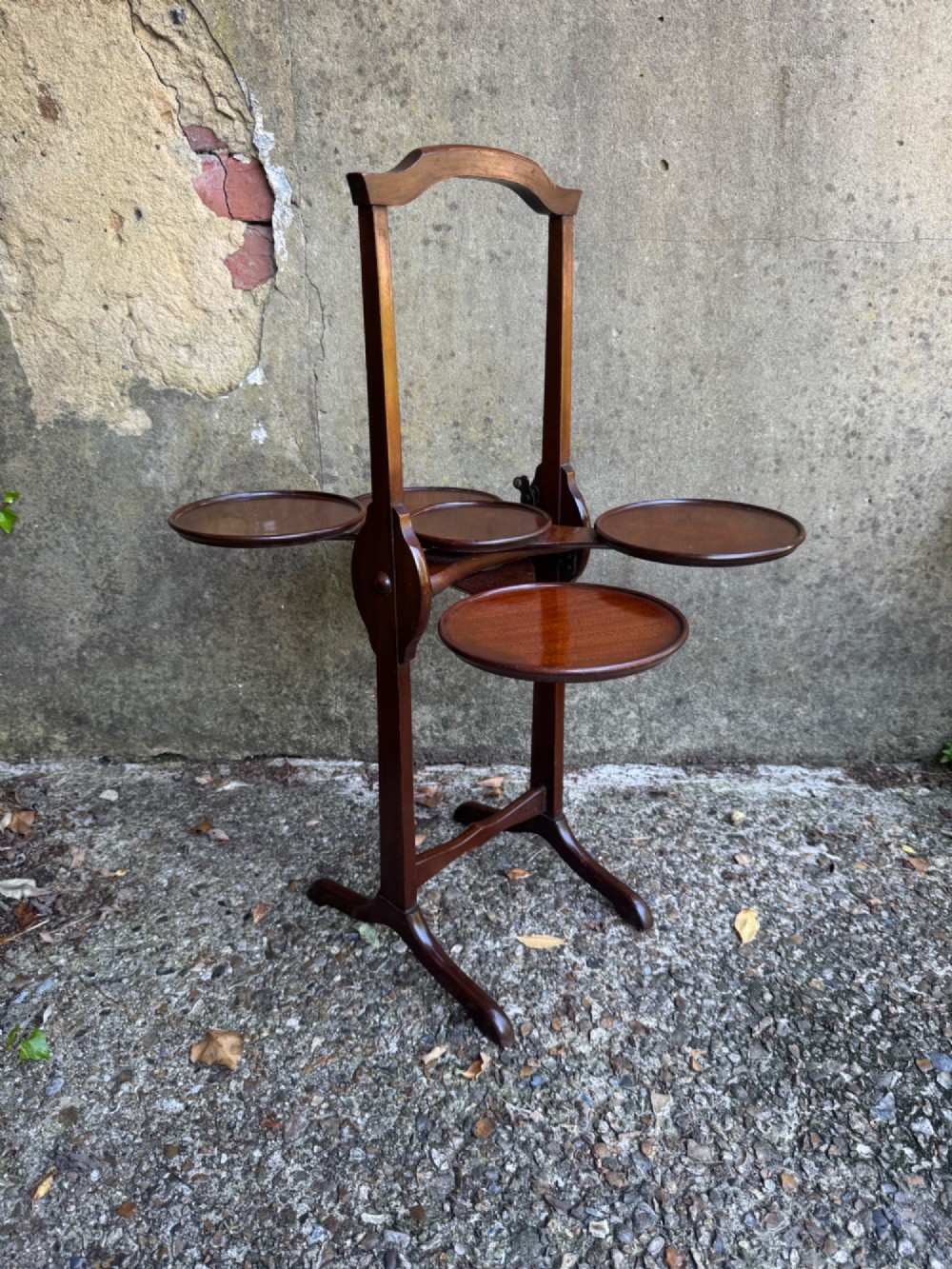An antique mahogany monoplane folding cake stand with five circular wooden trays supported on a vertical frame with arched feet. View XV