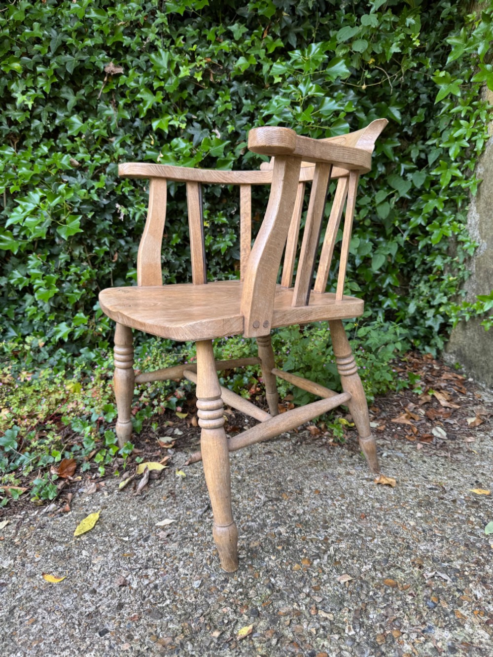 A low-backed antique oak captains armchair featuring turned legs, an H-stretcher, and vertical spindles supporting a broad curved armrest rail.