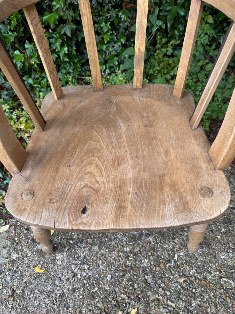 A low-backed antique oak captains armchair featuring turned legs, an H-stretcher, and vertical spindles supporting a broad curved armrest rail. View V
