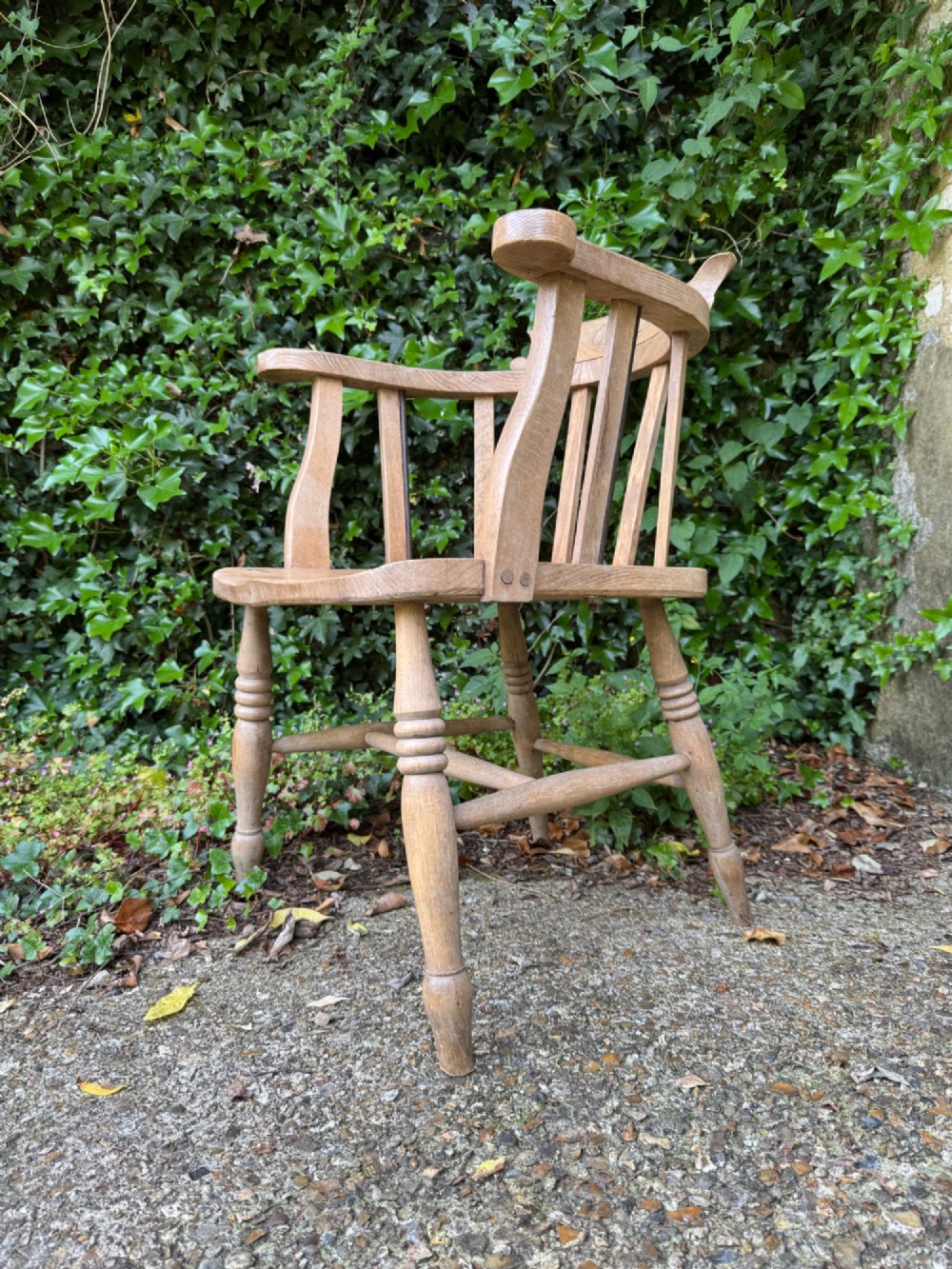 A low-backed antique oak captains armchair featuring turned legs, an H-stretcher, and vertical spindles supporting a broad curved armrest rail. View VII