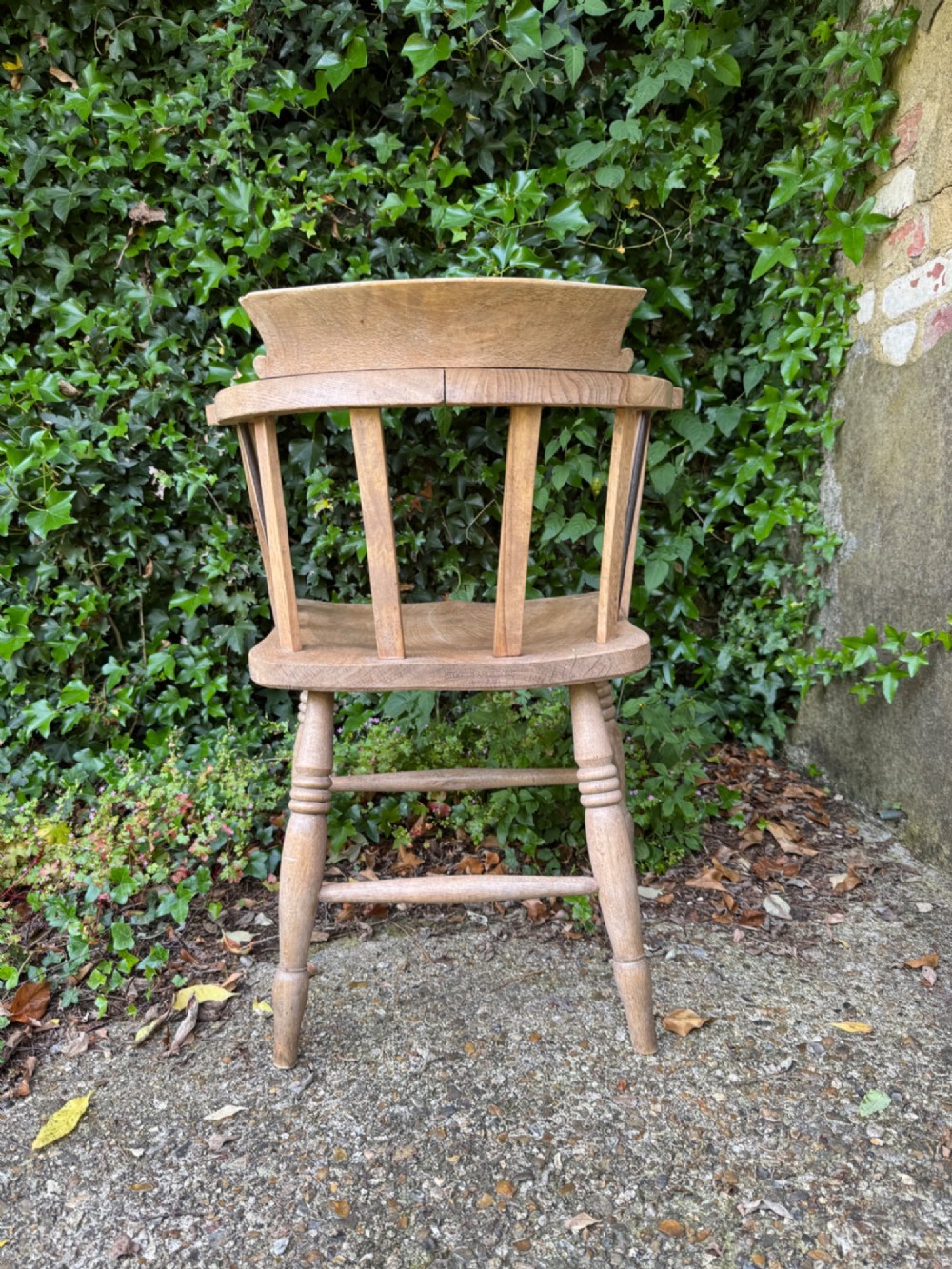 A low-backed antique oak captains armchair featuring turned legs, an H-stretcher, and vertical spindles supporting a broad curved armrest rail. View X