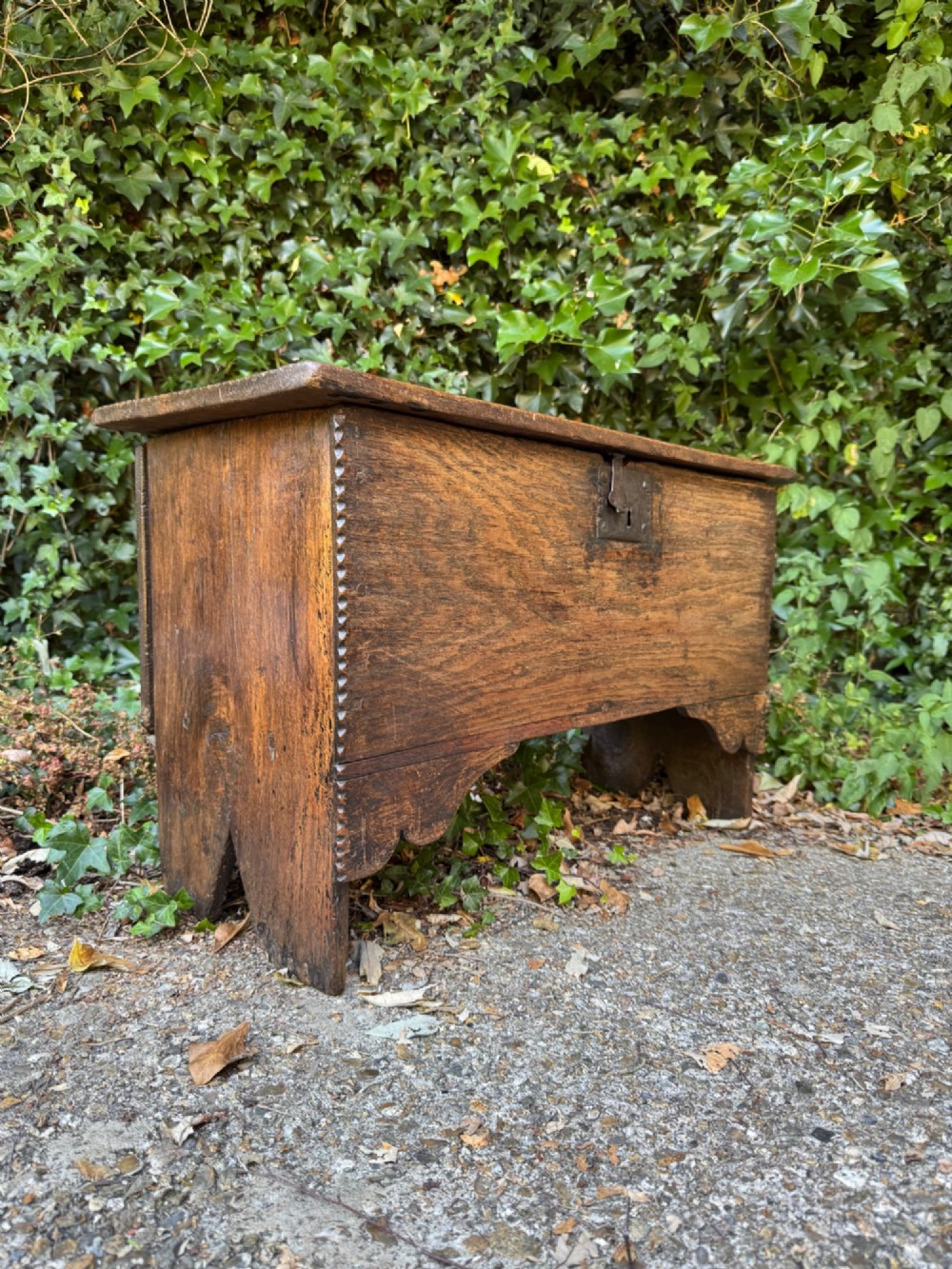 An antique dark oak plank coffer featuring notch-carved vertical edges, V-cut end feet, and a central iron lockplate.