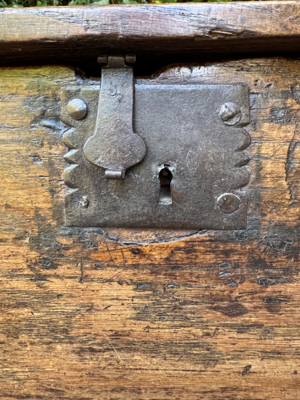 An antique dark oak plank coffer featuring notch-carved vertical edges, V-cut end feet, and a central iron lockplate. View IV