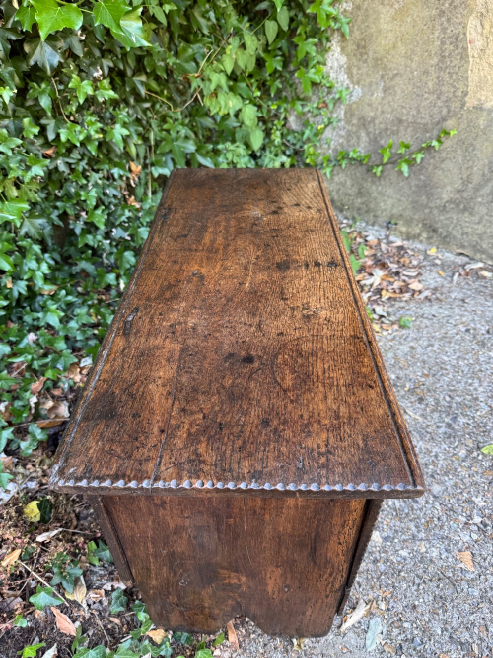 An antique dark oak plank coffer featuring notch-carved vertical edges, V-cut end feet, and a central iron lockplate. View VIII