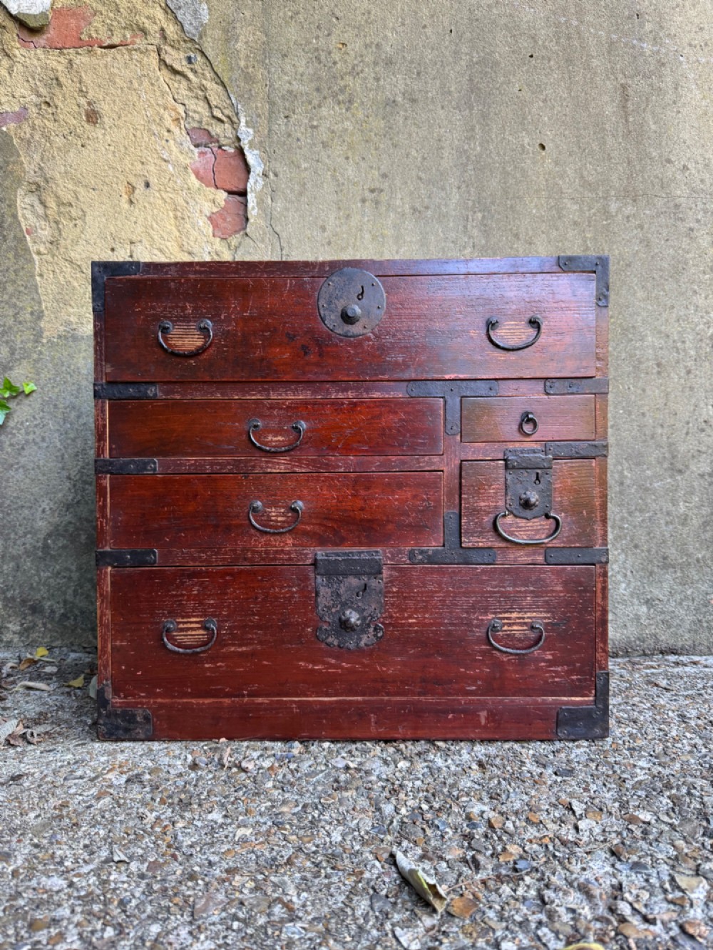 A reddish brown lacquered Japanese wooden tansu chest featuring iron corner plates, circular lock fittings, side carrying handles, and multiple graduated drawers. View II