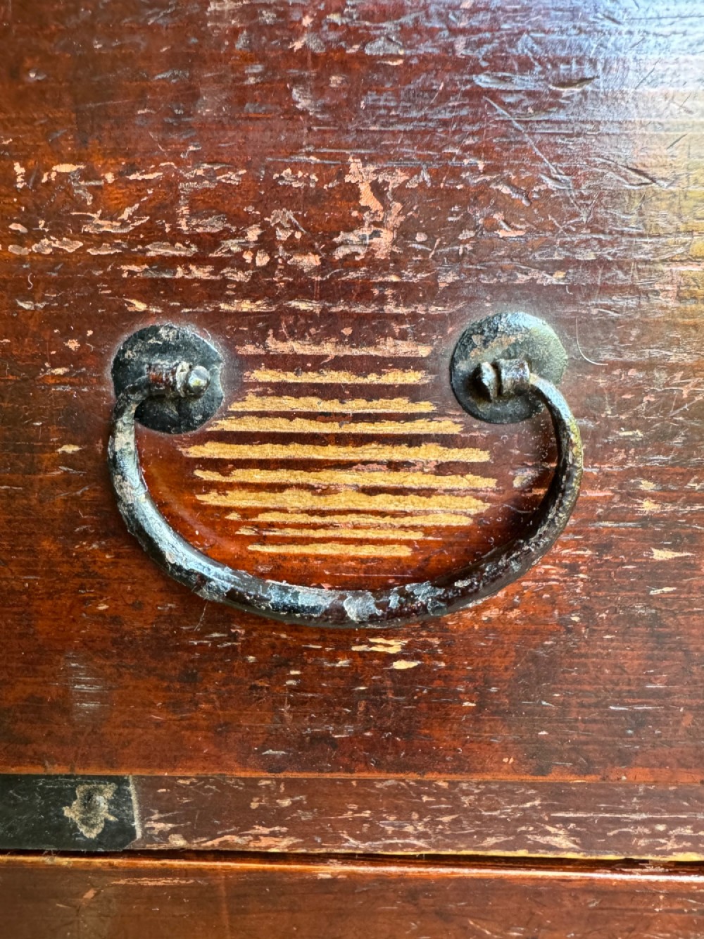 A reddish brown lacquered Japanese wooden tansu chest featuring iron corner plates, circular lock fittings, side carrying handles, and multiple graduated drawers. View V