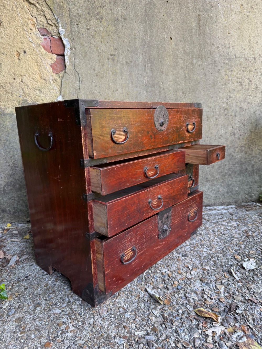A reddish brown lacquered Japanese wooden tansu chest featuring iron corner plates, circular lock fittings, side carrying handles, and multiple graduated drawers. View XI