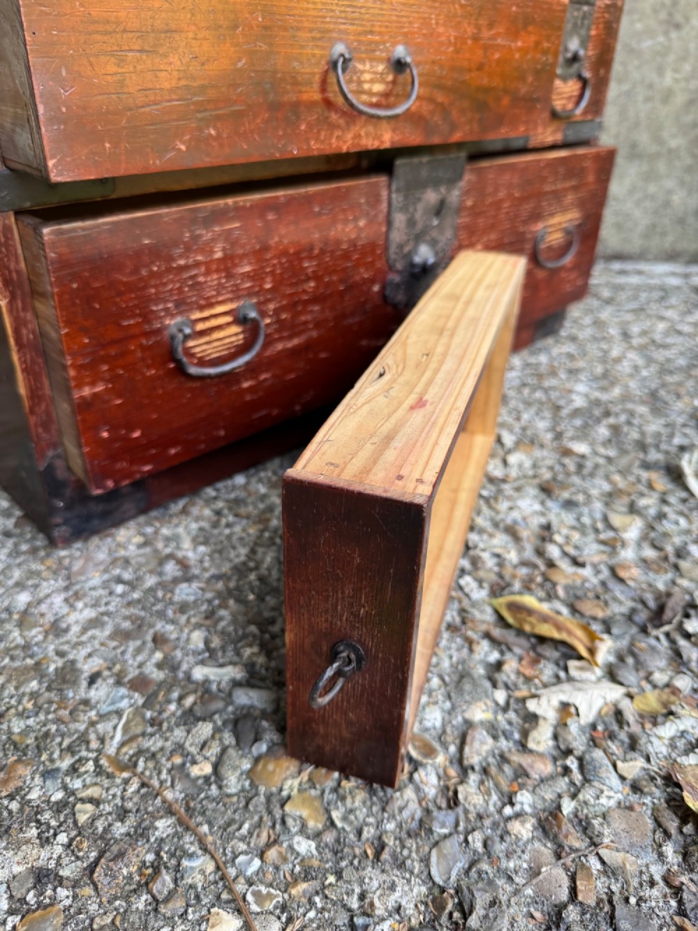 A reddish brown lacquered Japanese wooden tansu chest featuring iron corner plates, circular lock fittings, side carrying handles, and multiple graduated drawers. View XII