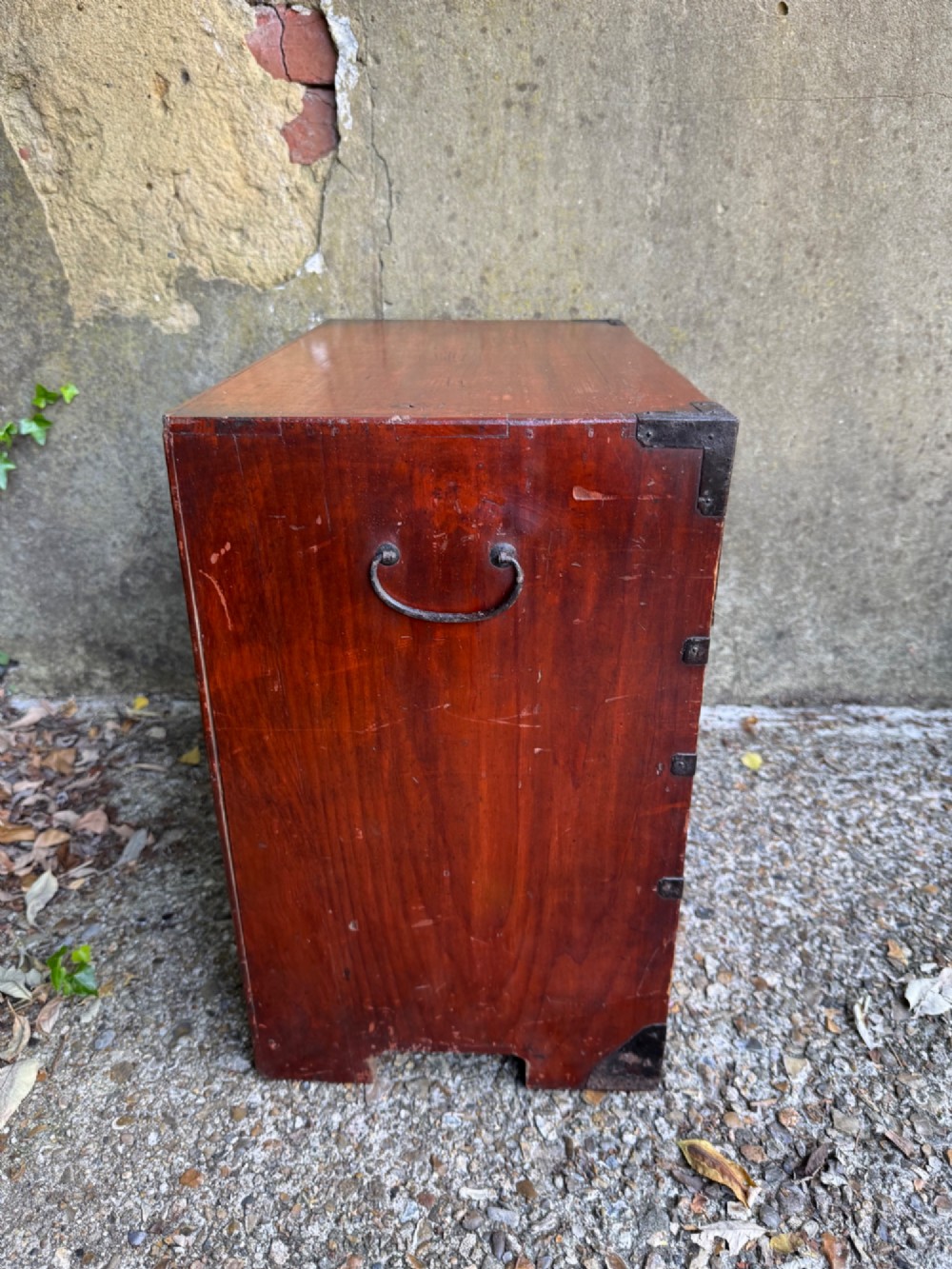 A reddish brown lacquered Japanese wooden tansu chest featuring iron corner plates, circular lock fittings, side carrying handles, and multiple graduated drawers. View XIII