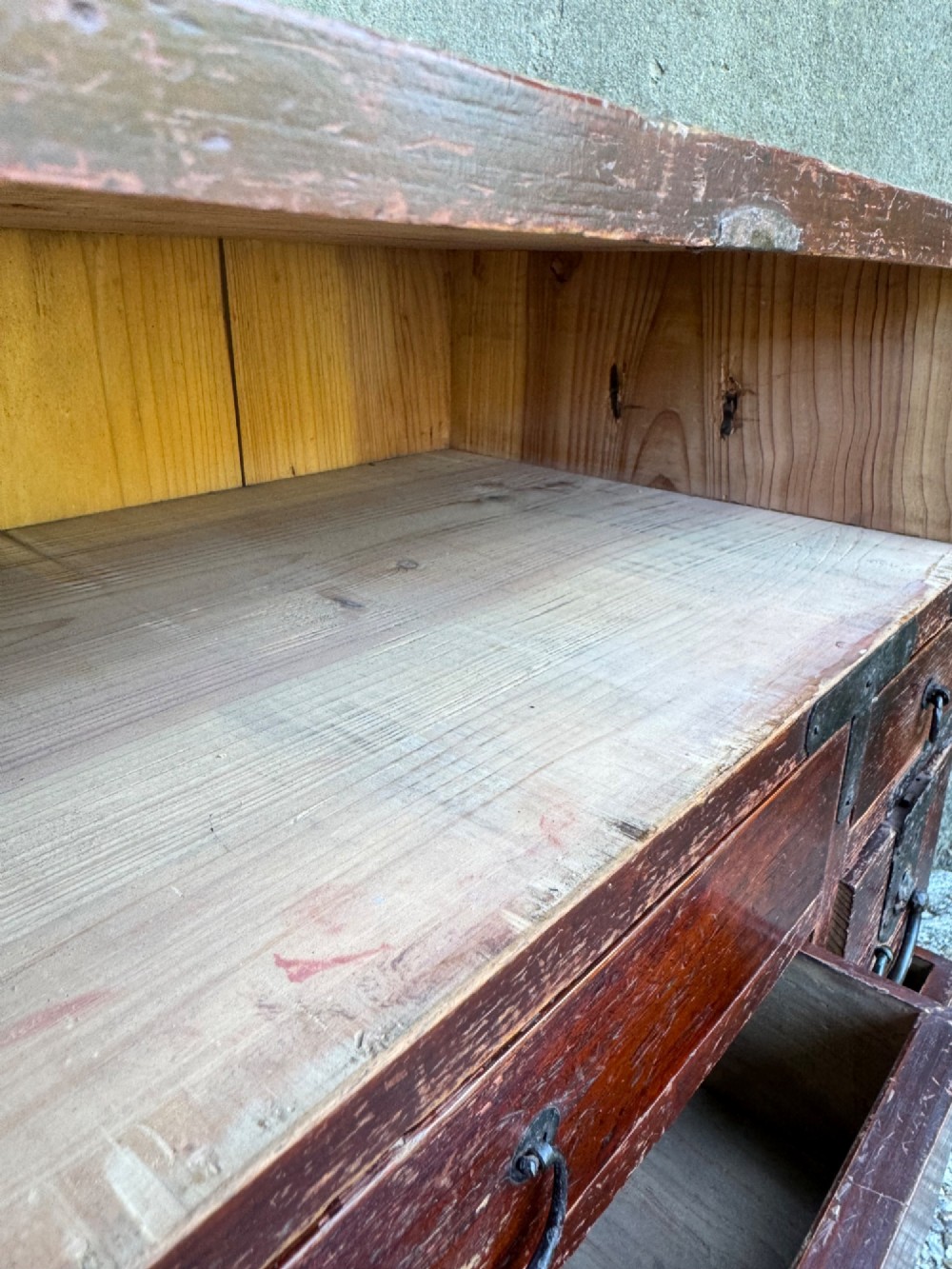 A reddish brown lacquered Japanese wooden tansu chest featuring iron corner plates, circular lock fittings, side carrying handles, and multiple graduated drawers. View XV