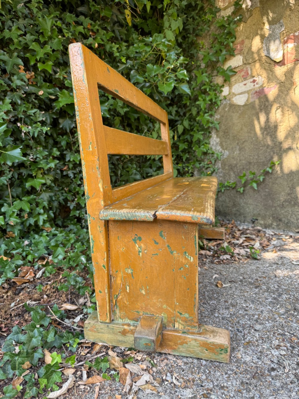 An antique rustic pine bench with a horizontal slat back, distressed mustard yellow painted finish, and solid end supports joined by a lower stretcher. View XI