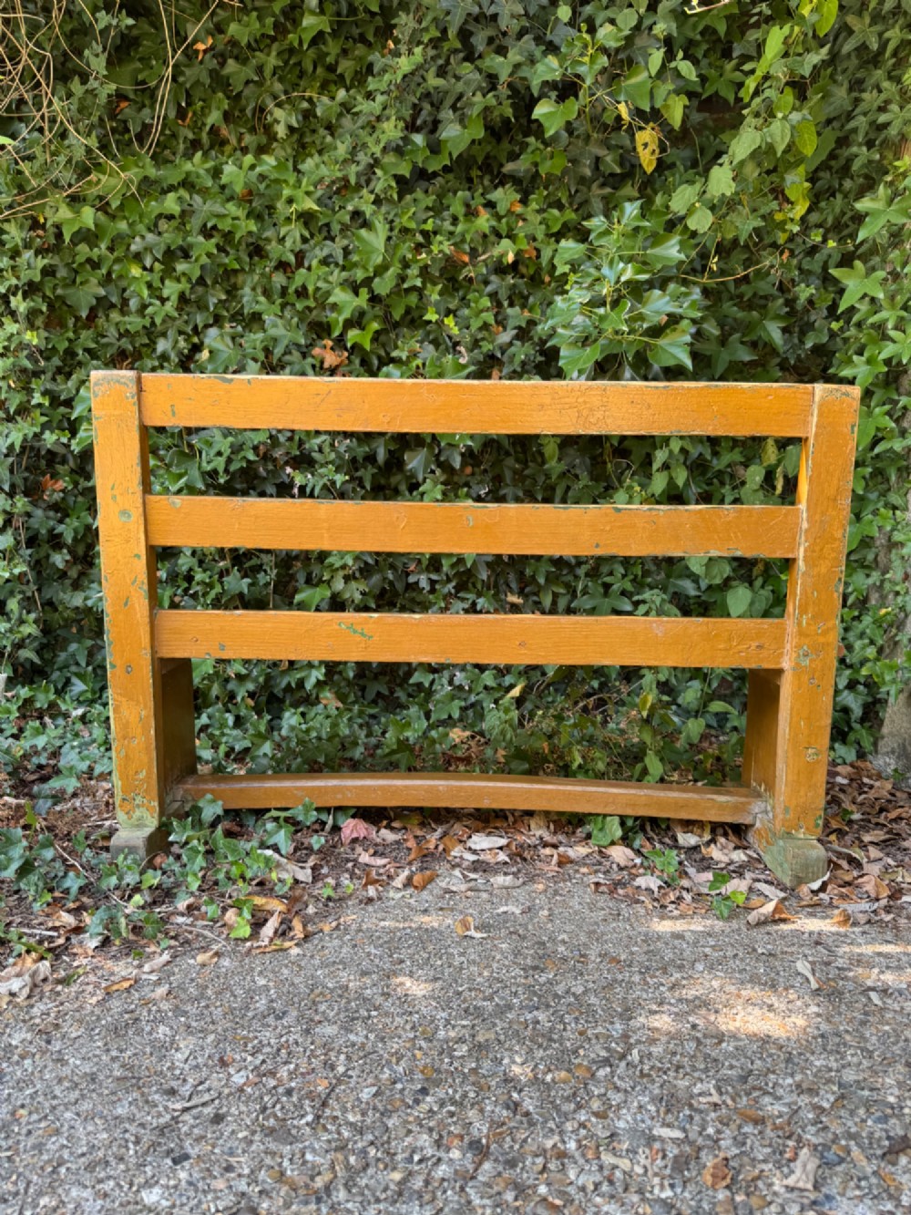 An antique rustic pine bench with a horizontal slat back, distressed mustard yellow painted finish, and solid end supports joined by a lower stretcher. View XIII