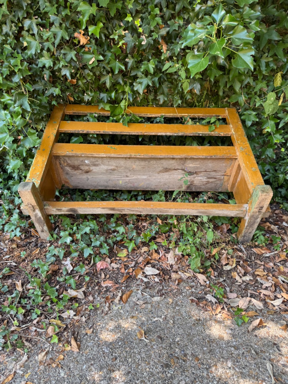 An antique rustic pine bench with a horizontal slat back, distressed mustard yellow painted finish, and solid end supports joined by a lower stretcher. View XV