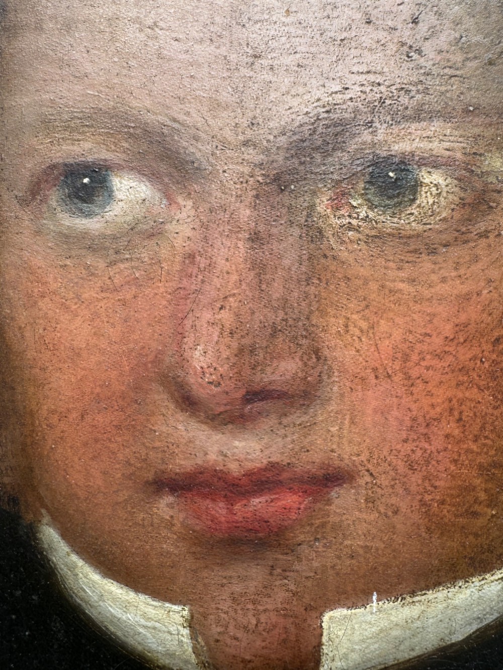 An unframed antique oil painting on canvas depicting a gentleman in a high black cravat and coat against a muted brown background. View V