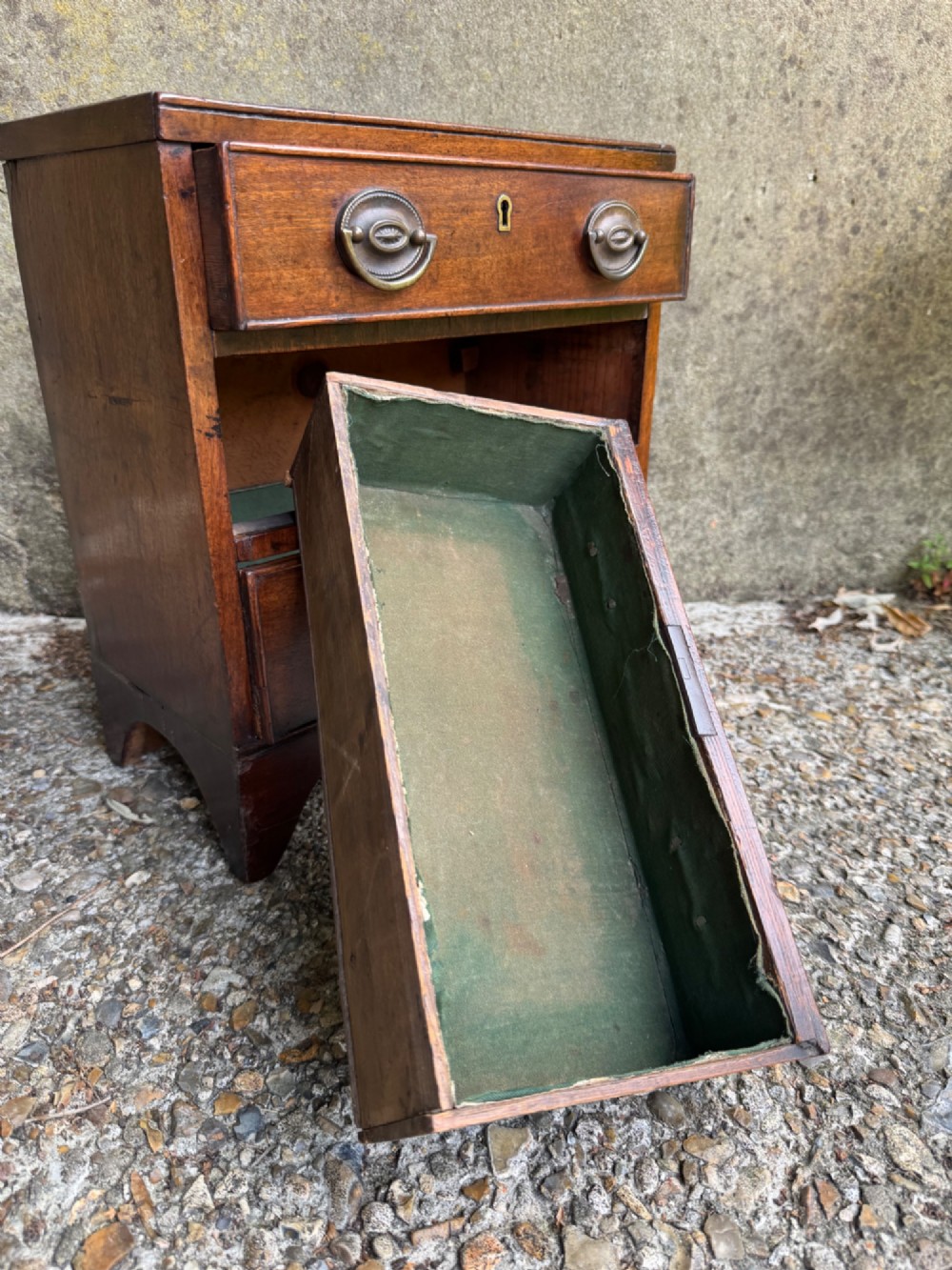 A miniature antique mahogany apprentice chest featuring three drawers with brass oval drop handles and keyhole escutcheons resting on a shaped apron base. View IX