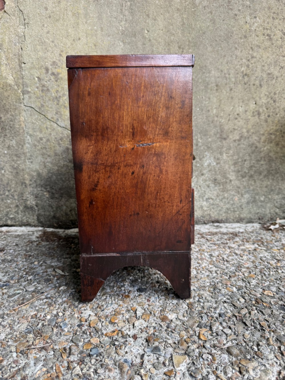 A miniature antique mahogany apprentice chest featuring three drawers with brass oval drop handles and keyhole escutcheons resting on a shaped apron base. View X