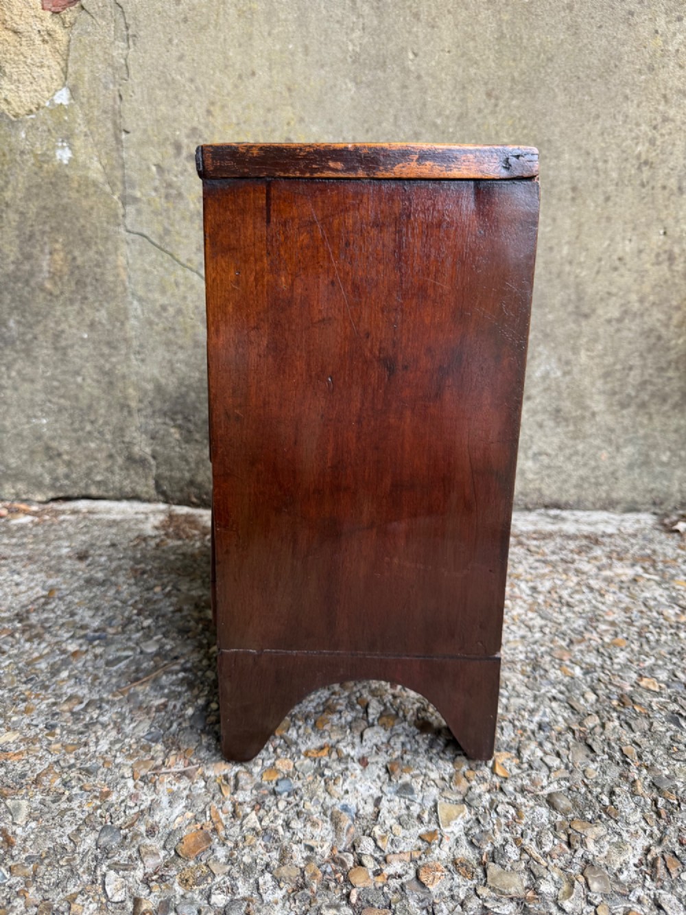 A miniature antique mahogany apprentice chest featuring three drawers with brass oval drop handles and keyhole escutcheons resting on a shaped apron base. View XI