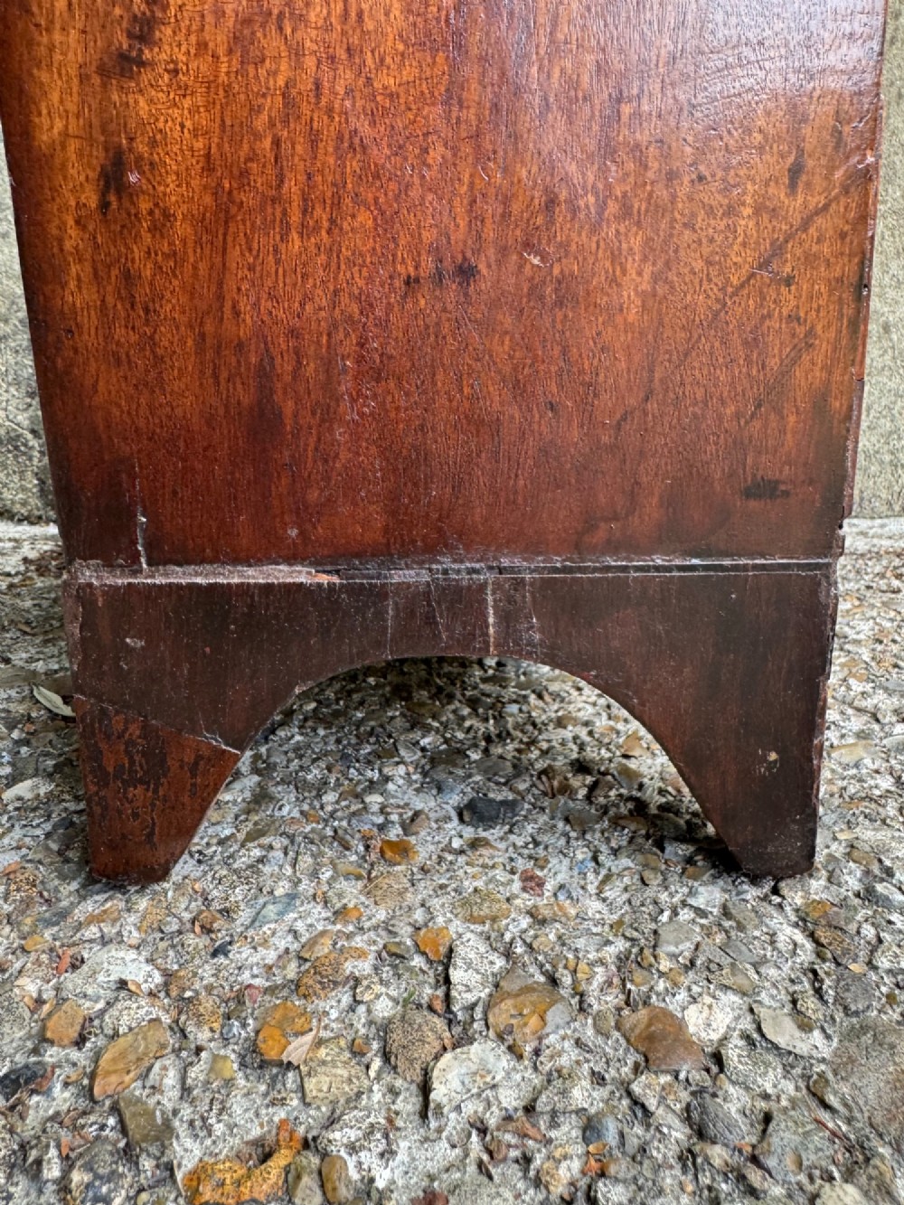 A miniature antique mahogany apprentice chest featuring three drawers with brass oval drop handles and keyhole escutcheons resting on a shaped apron base. View XII