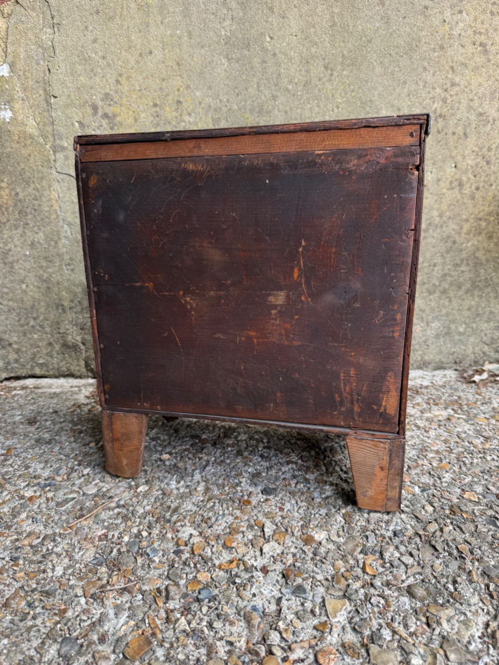 A miniature antique mahogany apprentice chest featuring three drawers with brass oval drop handles and keyhole escutcheons resting on a shaped apron base. View XIII