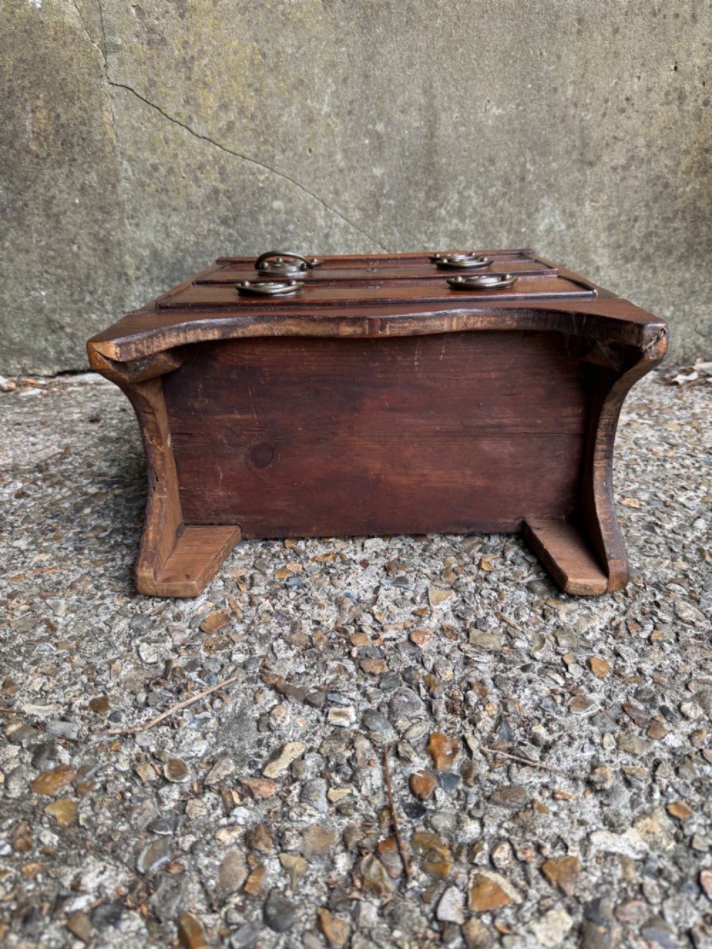 A miniature antique mahogany apprentice chest featuring three drawers with brass oval drop handles and keyhole escutcheons resting on a shaped apron base. View XIV
