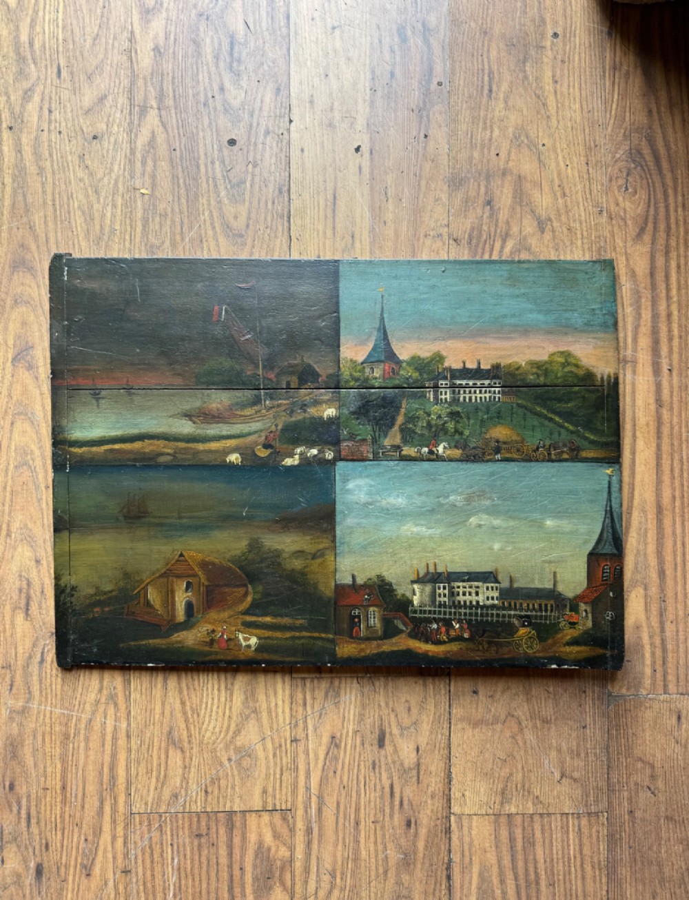 A rectangular antique wooden panel featuring four distinct naive painted oil scenes depicting churches, country houses, sailing ships, and pastoral landscapes.