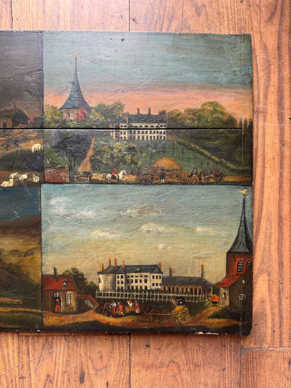 A rectangular antique wooden panel featuring four distinct naive painted oil scenes depicting churches, country houses, sailing ships, and pastoral landscapes. View II