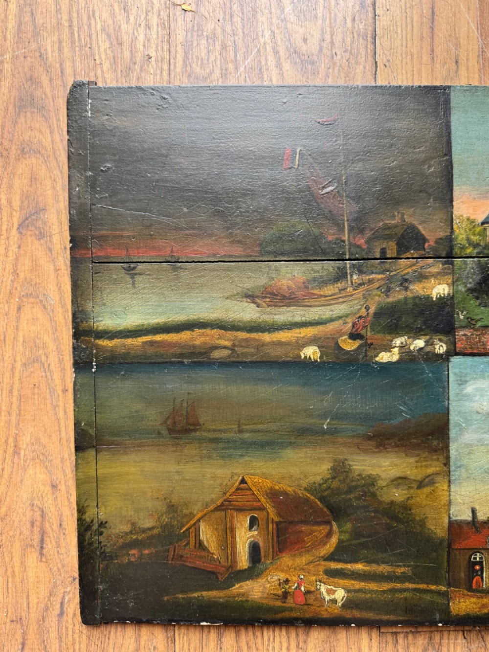 A rectangular antique wooden panel featuring four distinct naive painted oil scenes depicting churches, country houses, sailing ships, and pastoral landscapes. View III