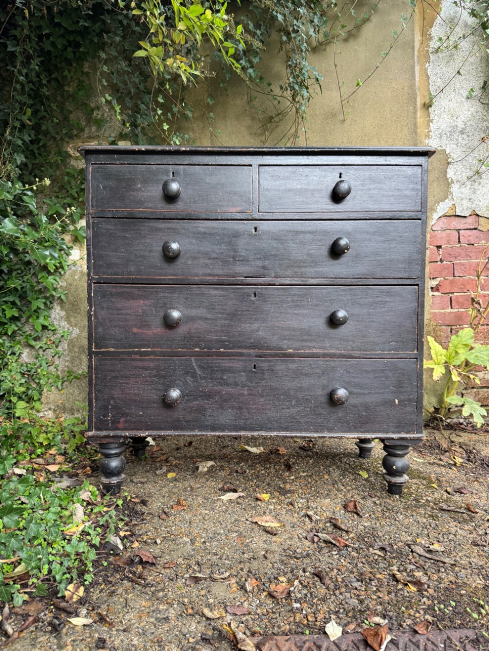 A Victorian dark painted pine chest featuring two short drawers above three long drawers, fitted with turned wooden knobs and supported by turned feet. View II
