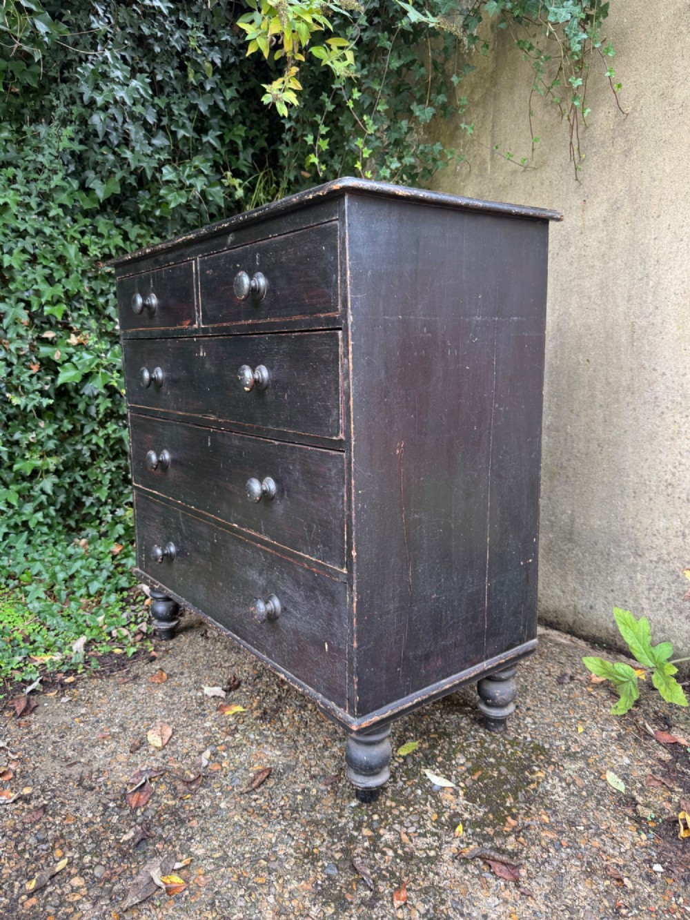 A Victorian dark painted pine chest featuring two short drawers above three long drawers, fitted with turned wooden knobs and supported by turned feet. View V
