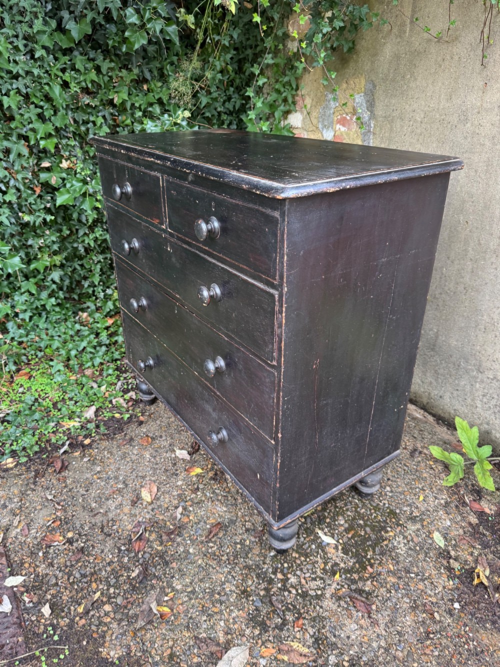 A Victorian dark painted pine chest featuring two short drawers above three long drawers, fitted with turned wooden knobs and supported by turned feet. View VII