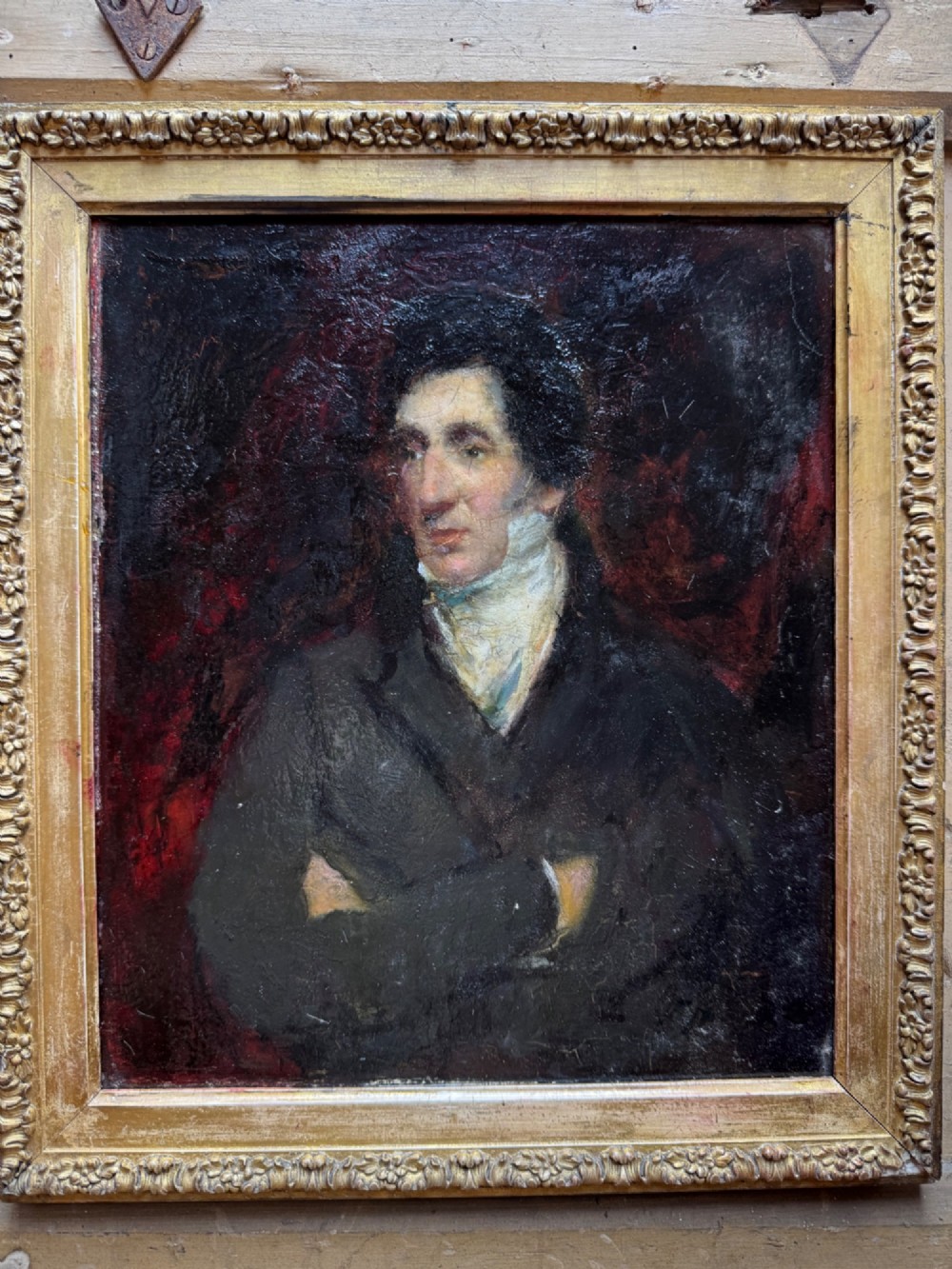 An antique oil painting depicting a gentleman with dark hair in a black coat against a deep red background, framed in a decorative gold leaf frame. View II