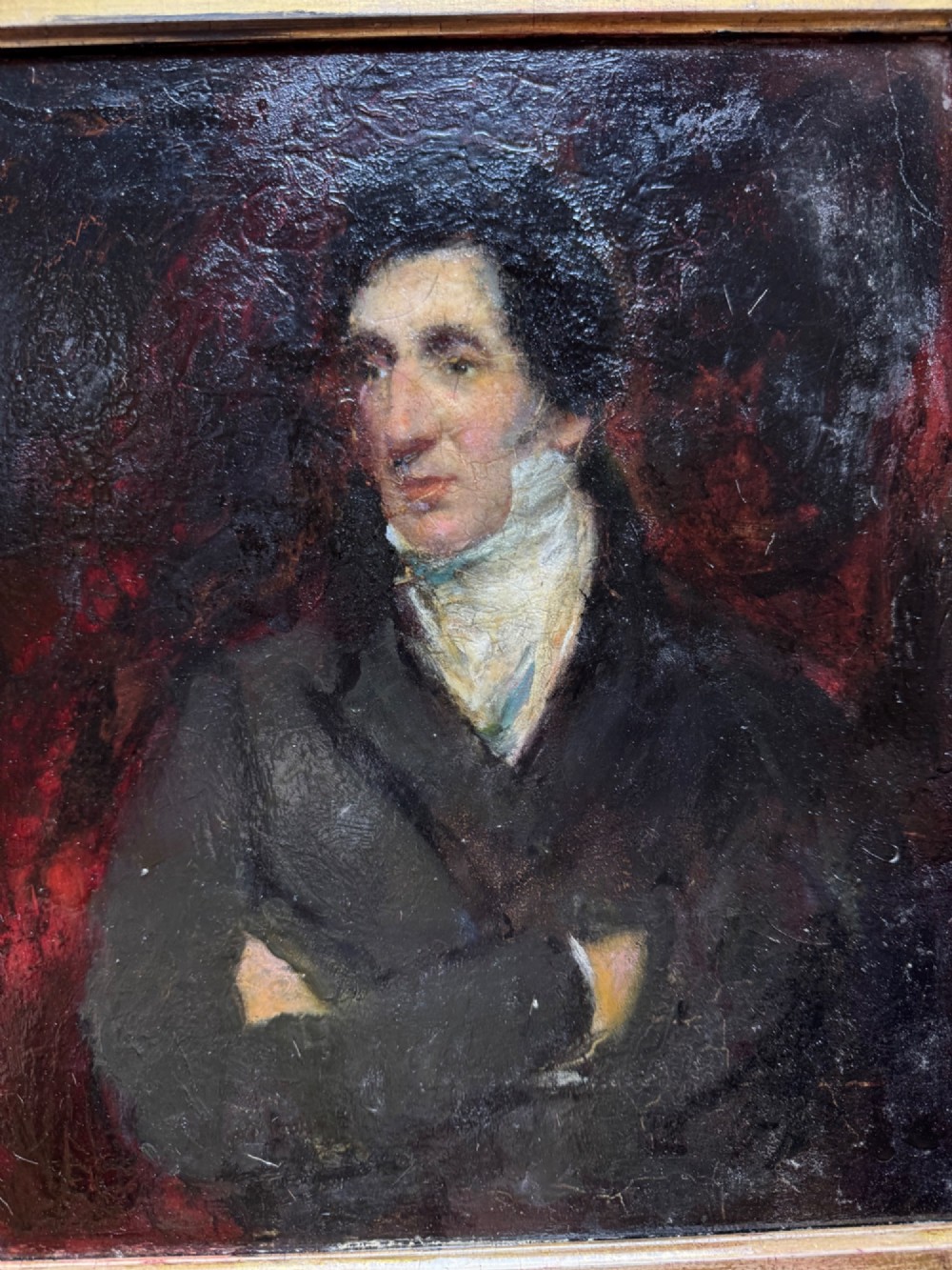 An antique oil painting depicting a gentleman with dark hair in a black coat against a deep red background, framed in a decorative gold leaf frame. View III