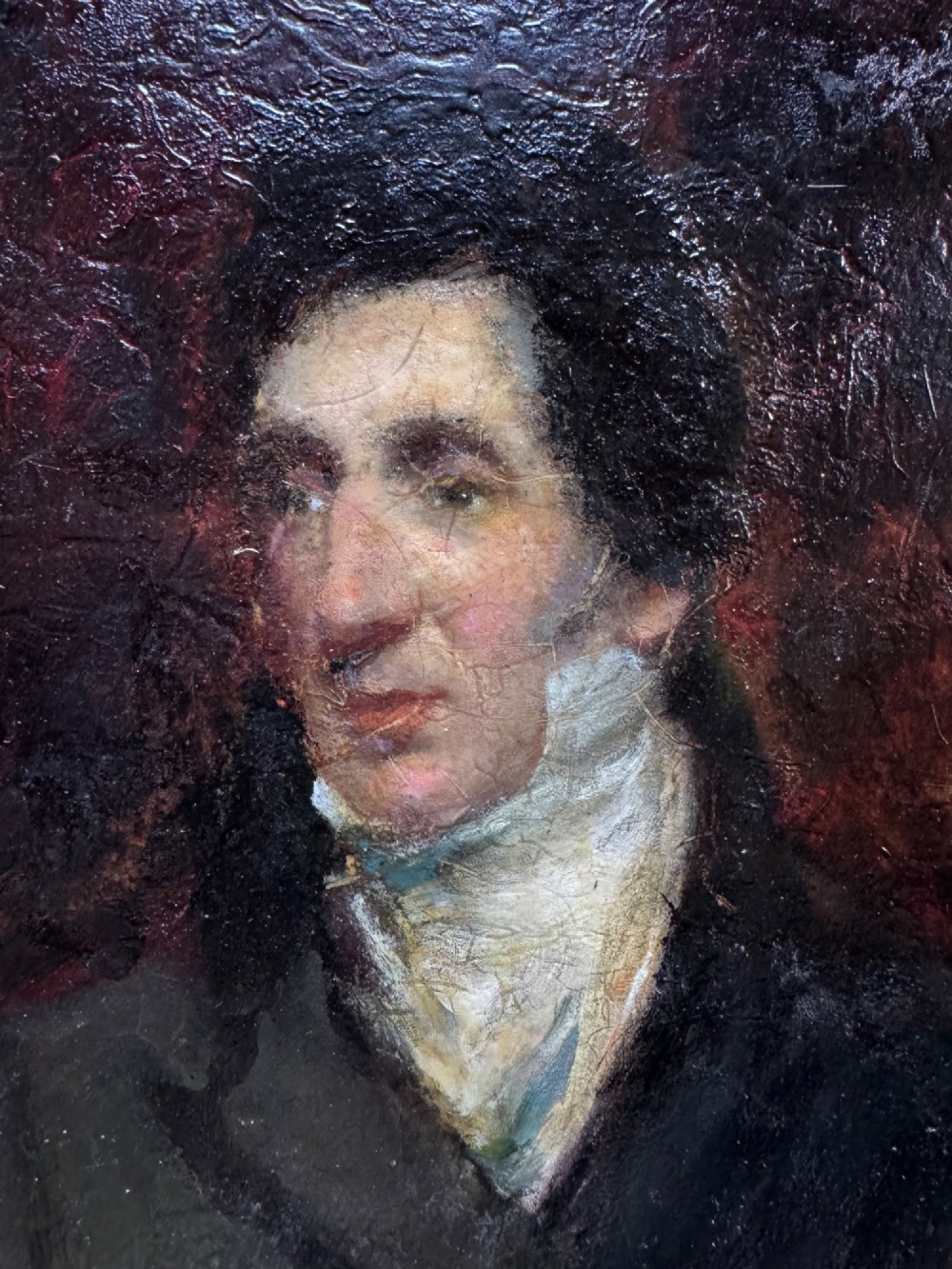 An antique oil painting depicting a gentleman with dark hair in a black coat against a deep red background, framed in a decorative gold leaf frame. View IV