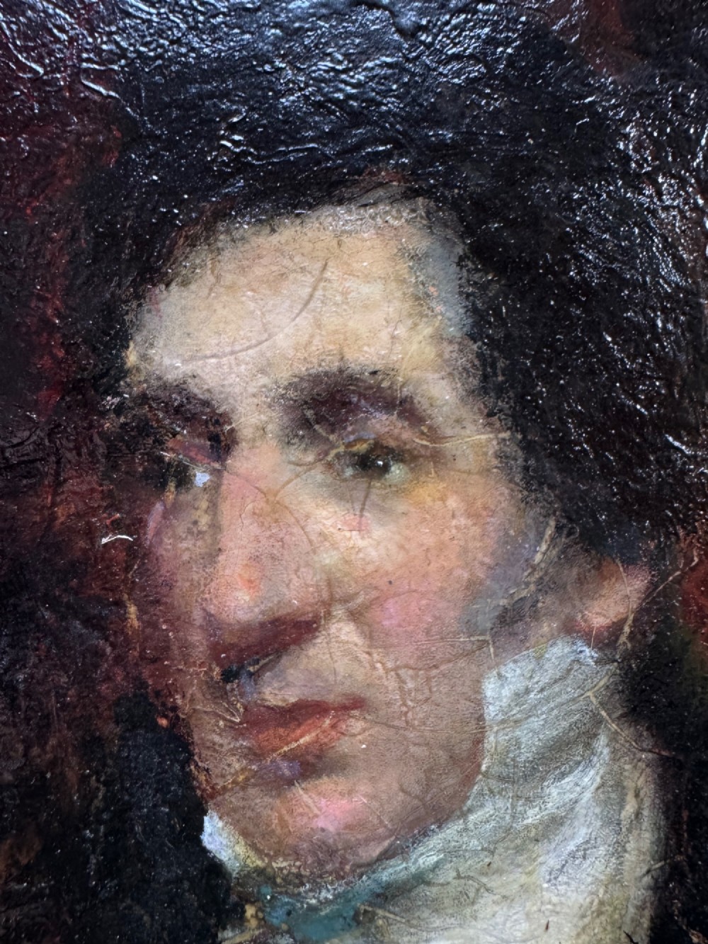 An antique oil painting depicting a gentleman with dark hair in a black coat against a deep red background, framed in a decorative gold leaf frame. View V