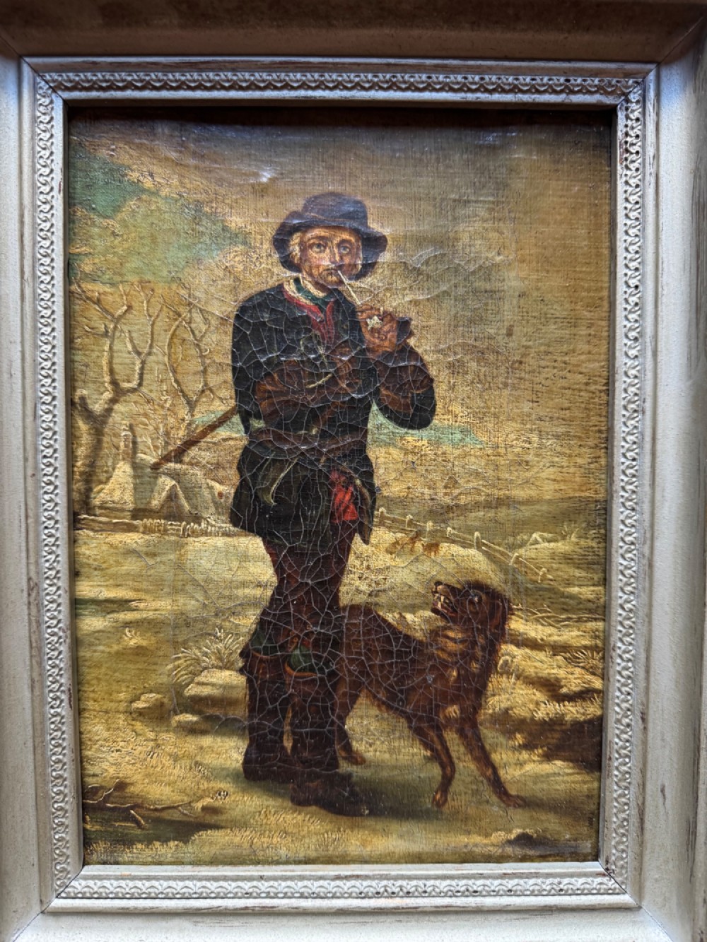 An antique oil painting depicting a standing man with a pipe and his dog in a countryside landscape, housed in a deep silvered moulded frame. View III