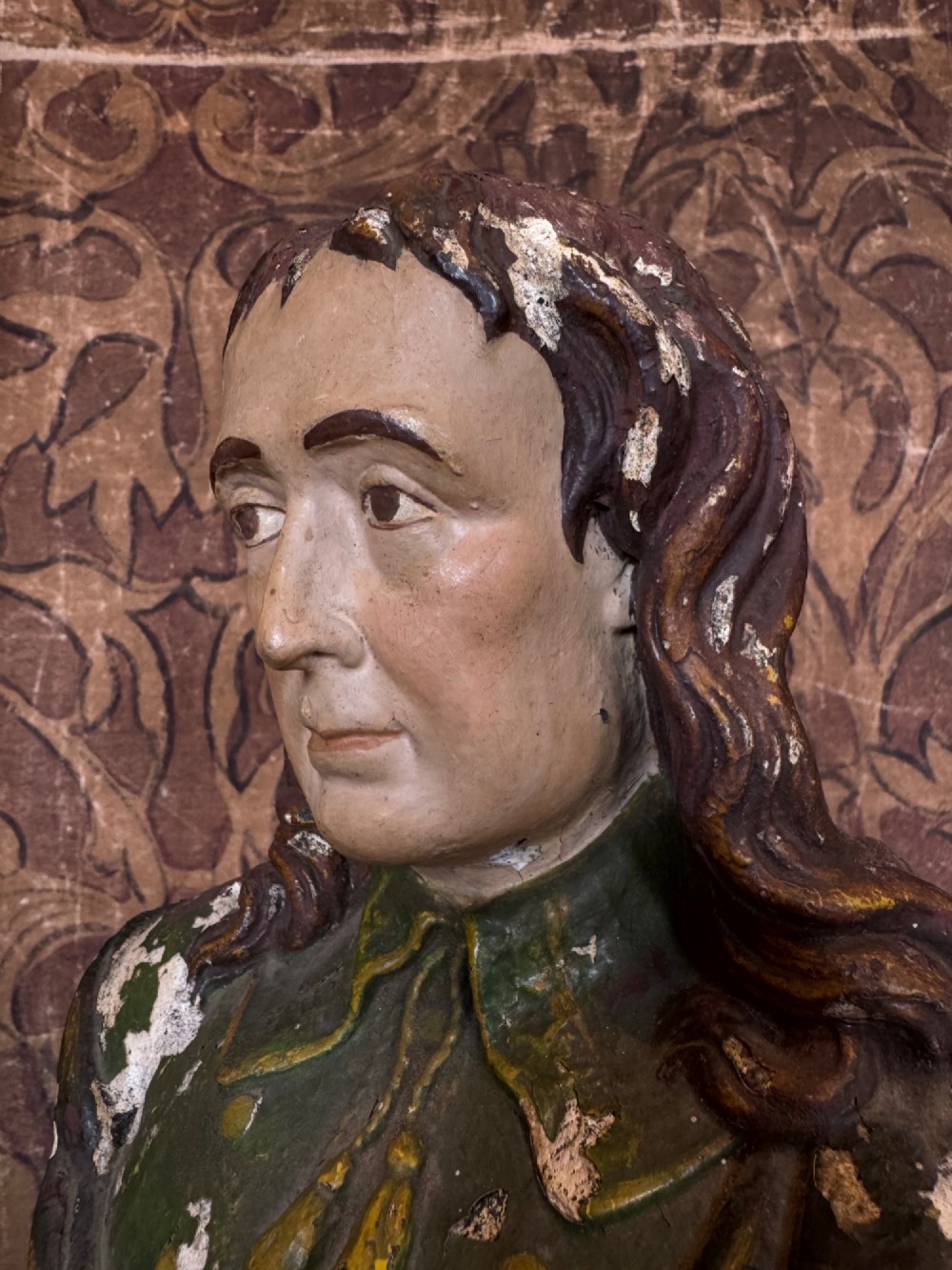 A polychrome painted bust depicting John Milton with long brown hair, a collared shirt with tassels, and a grey socle pedestal base. View III