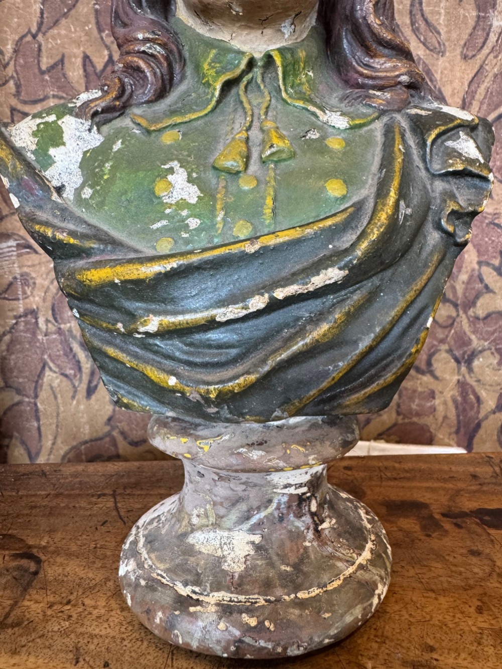 A polychrome painted bust depicting John Milton with long brown hair, a collared shirt with tassels, and a grey socle pedestal base. View V