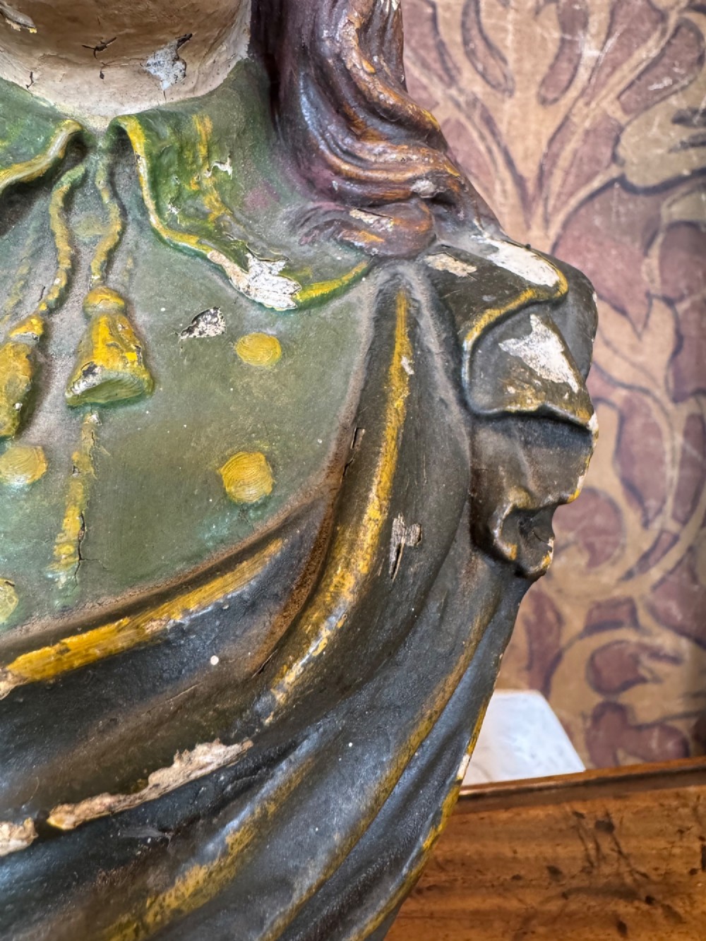 A polychrome painted bust depicting John Milton with long brown hair, a collared shirt with tassels, and a grey socle pedestal base. View VI