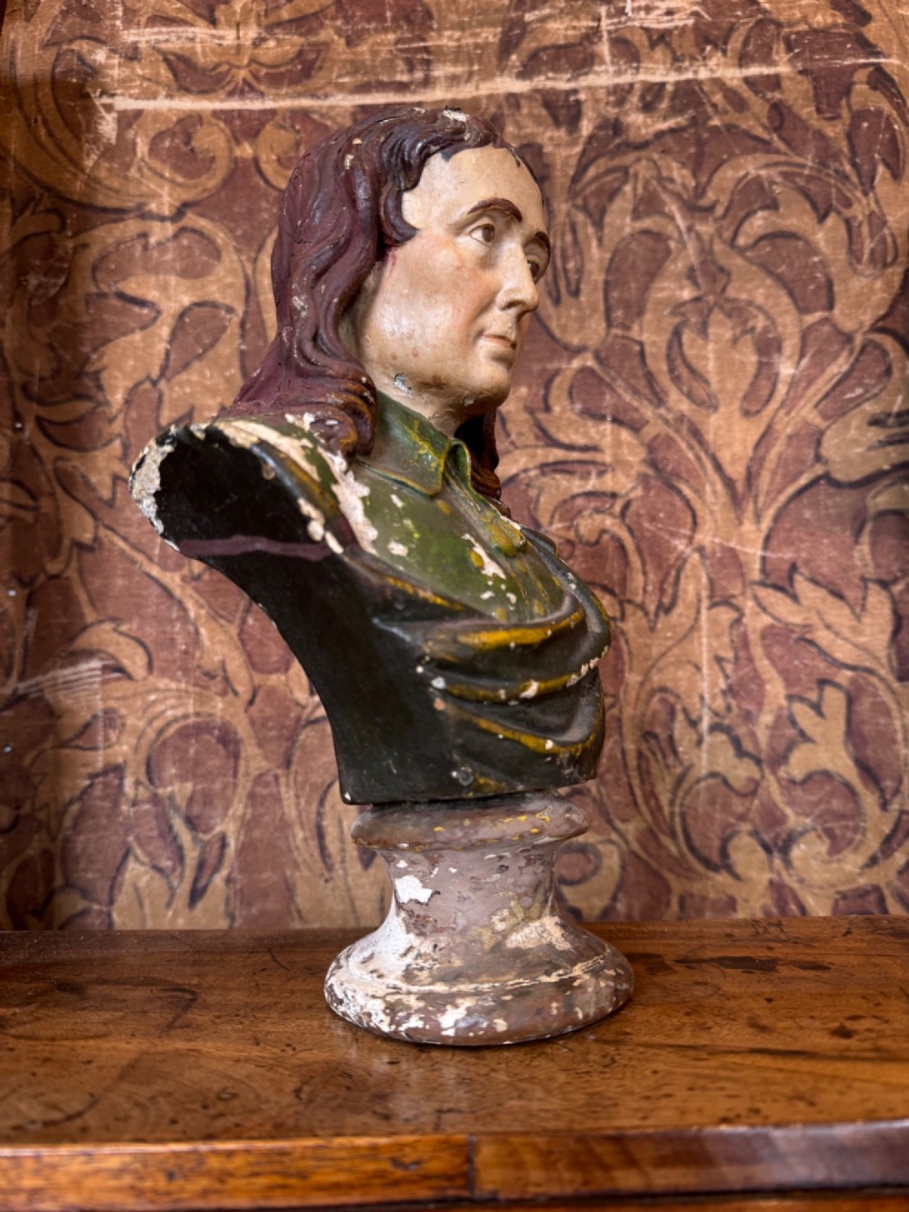 A polychrome painted bust depicting John Milton with long brown hair, a collared shirt with tassels, and a grey socle pedestal base. View VII