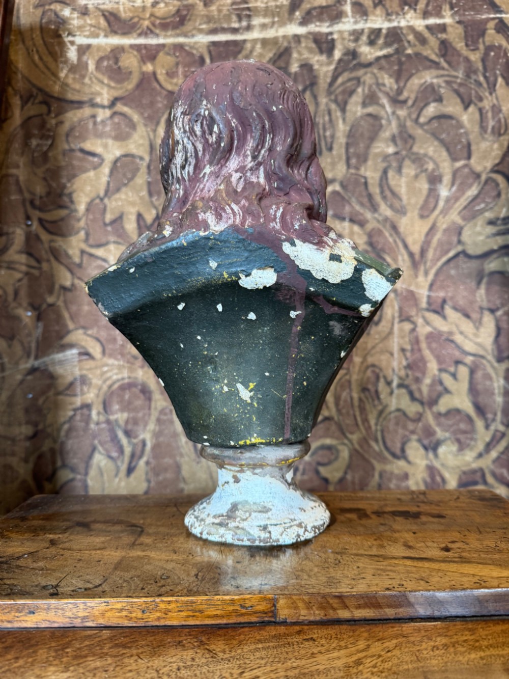 A polychrome painted bust depicting John Milton with long brown hair, a collared shirt with tassels, and a grey socle pedestal base. View IX