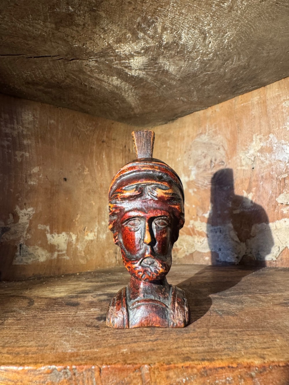 A hand-carved dark wood bust depicting a bearded warrior wearing a crested classical helmet in profile. View III