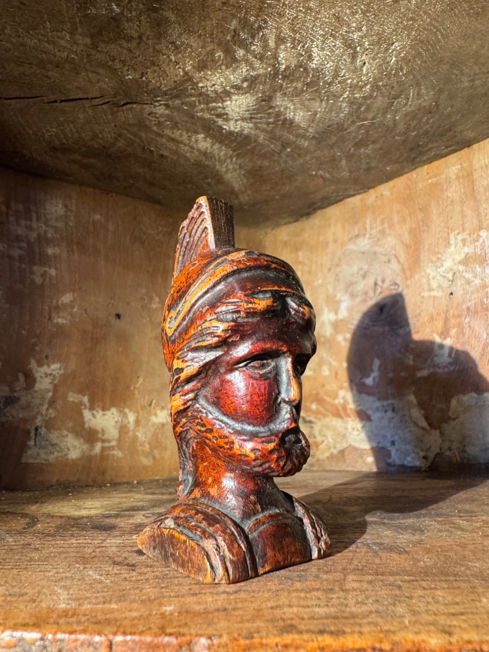 A hand-carved dark wood bust depicting a bearded warrior wearing a crested classical helmet in profile. View IV