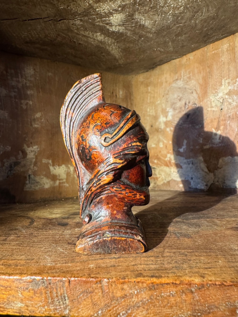 A hand-carved dark wood bust depicting a bearded warrior wearing a crested classical helmet in profile. View V