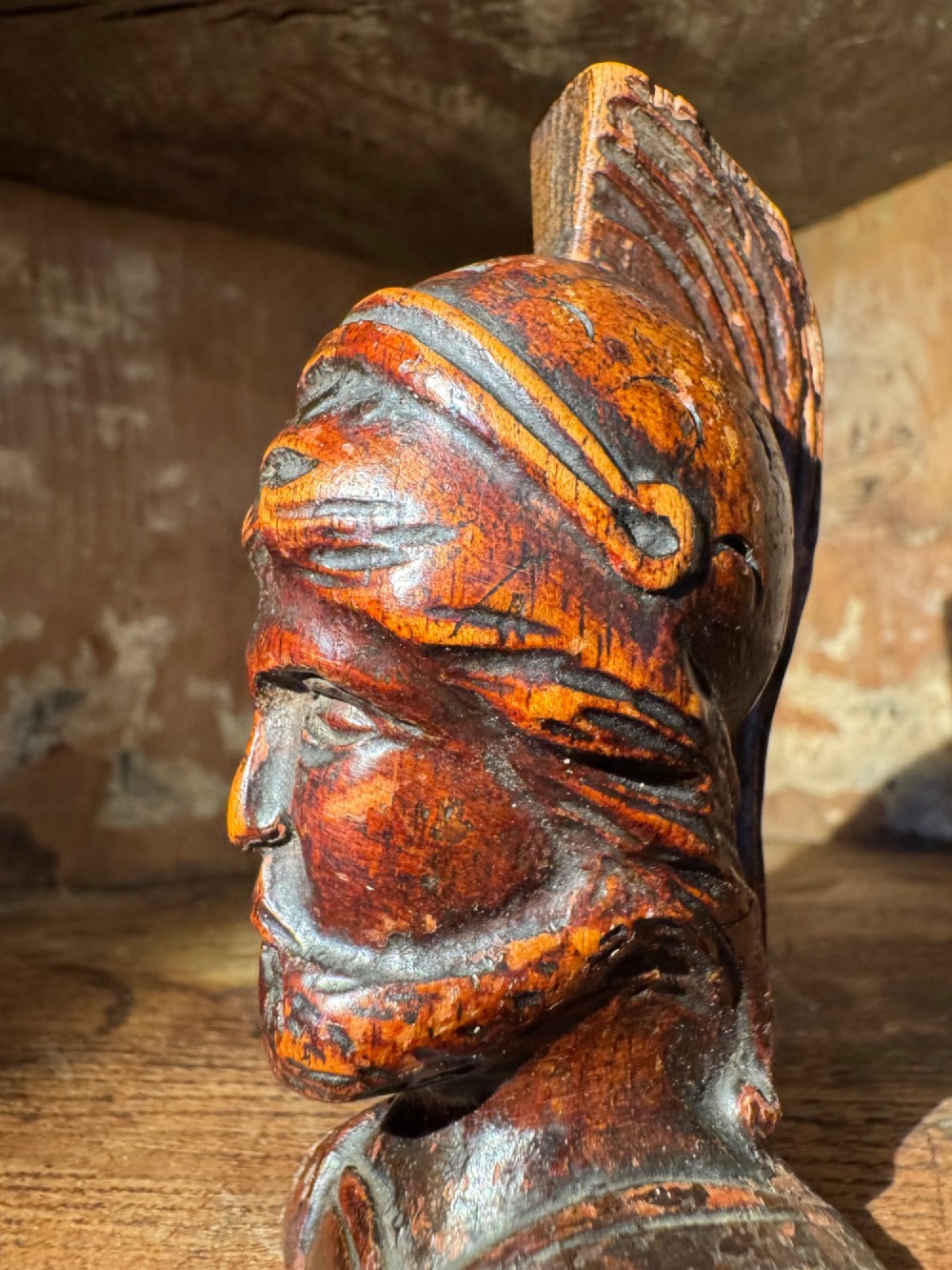 A hand-carved dark wood bust depicting a bearded warrior wearing a crested classical helmet in profile. View IX