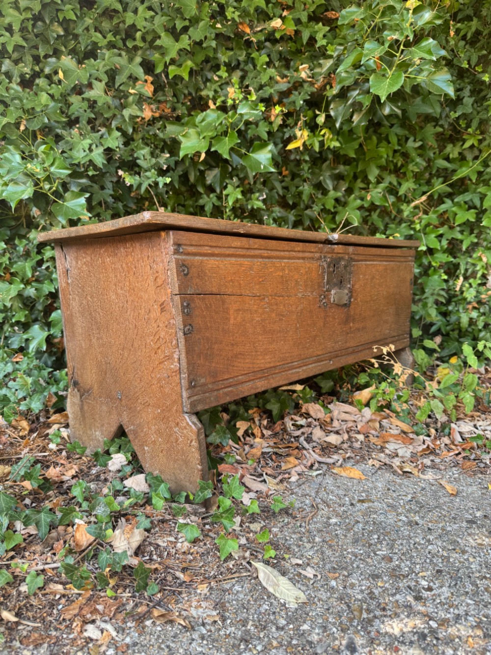 An early oak plank coffer featuring notched end panels, a hinged lid, horizontal moulding, and an iron lockplate.