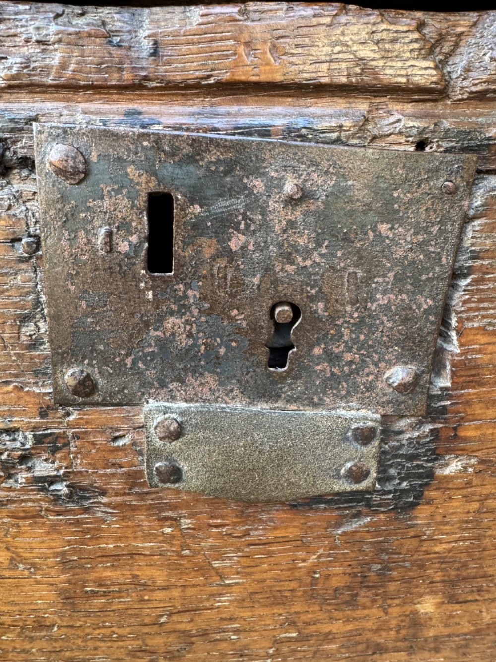 An early oak plank coffer featuring notched end panels, a hinged lid, horizontal moulding, and an iron lockplate. View V
