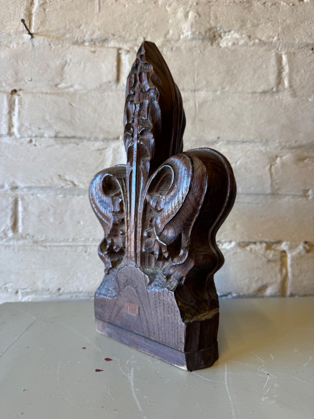 A hand-carved dark oak poppy head finial featuring intricate Gothic leaf motifs standing vertically.